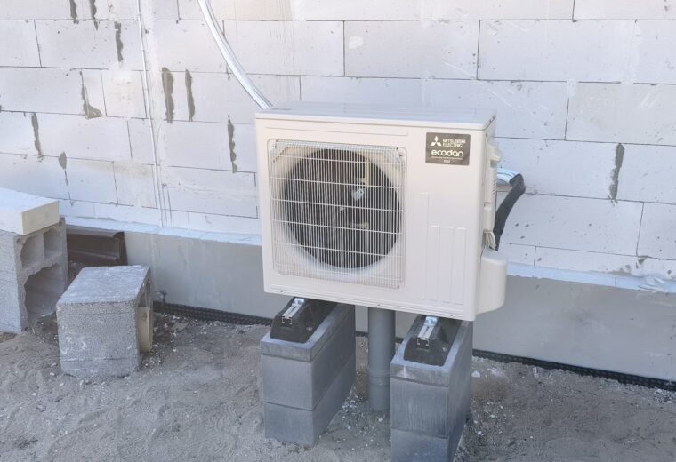 Jednostka zewnętrzna pompy ciepła Mitsubishi Electric na podstawie przy ścianie budynku — montaż Ekoinstal